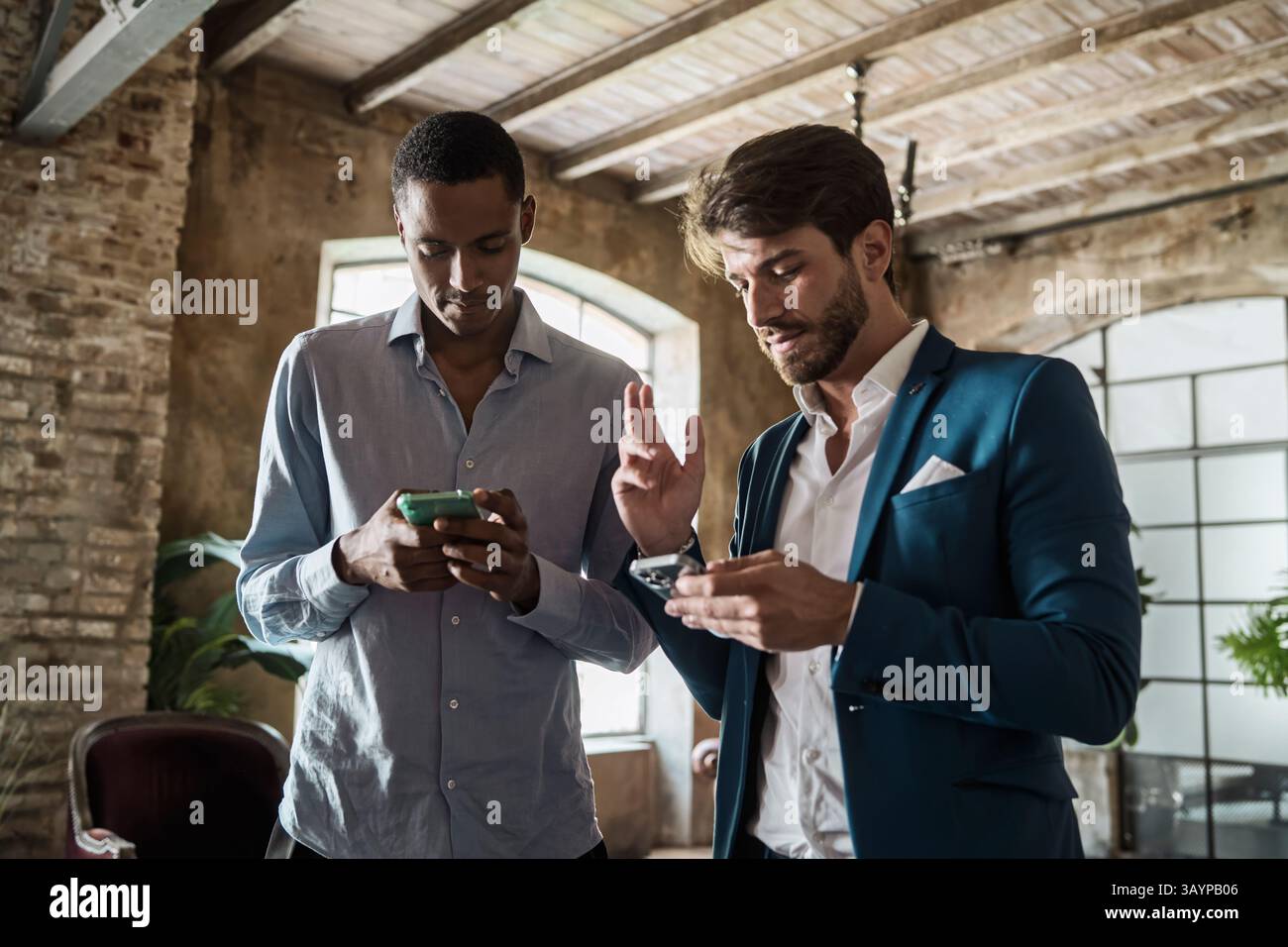 Two diverse businessmen using smartphones in a modern loft office ...