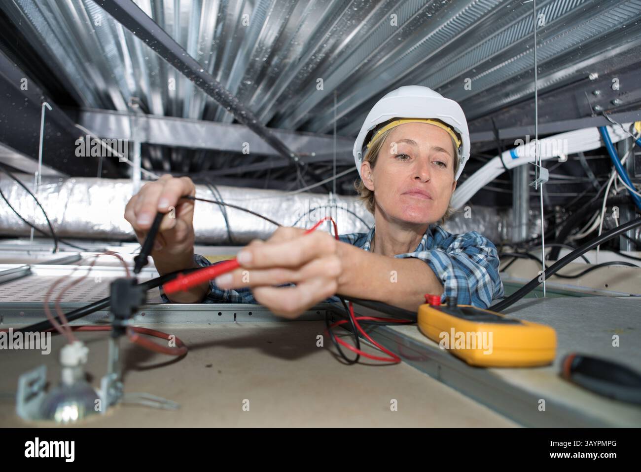 female electrician testing charge to spotlight Stock Photo