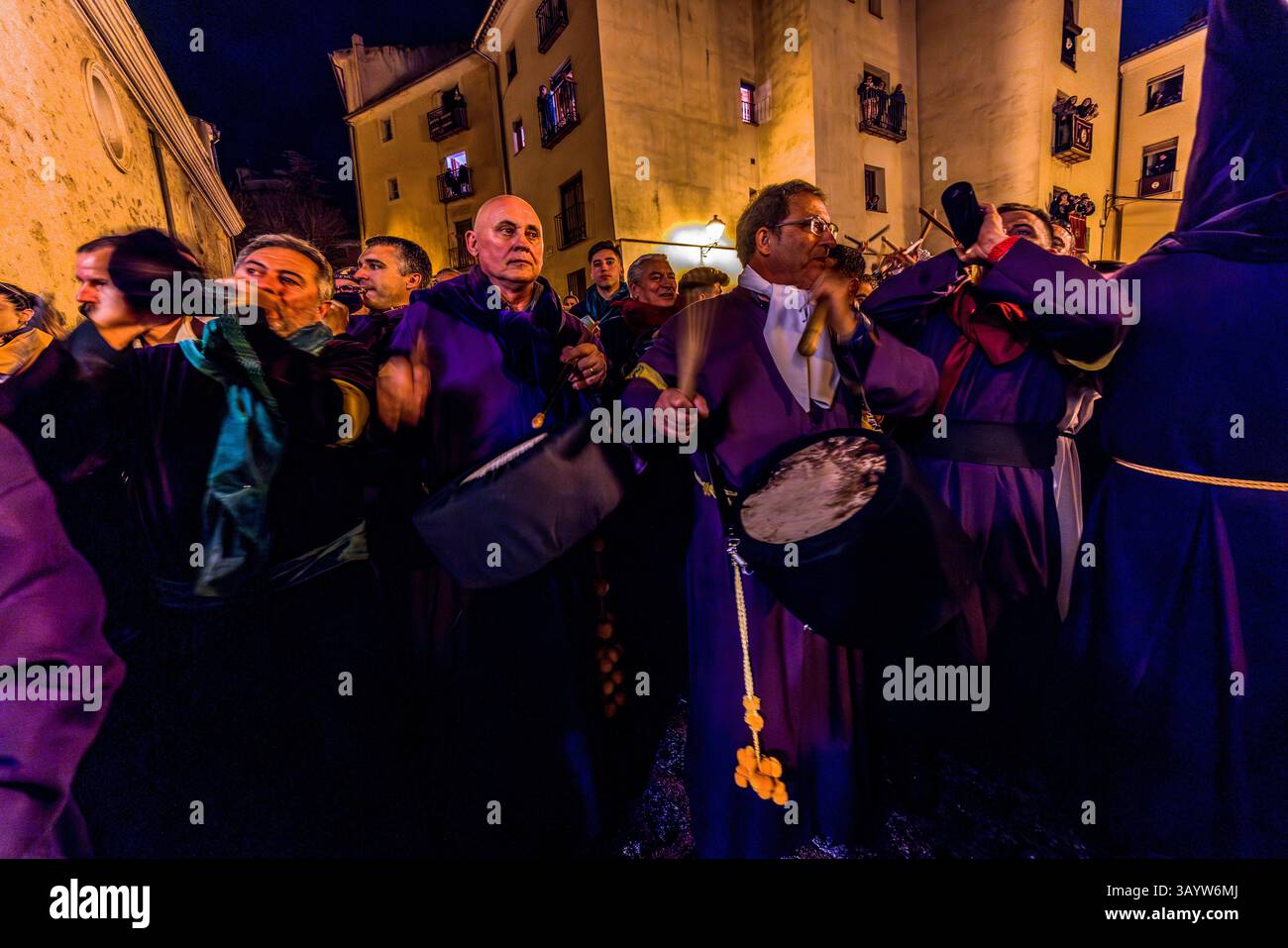 The Turbas de Cuenca have stayed awake through the night of Good Friday. In front of the parish church of El Salvador, they beat drums and blow tin trumpets. The noise can be heard throughout Cuenca for hours before the procession begins. Plaza Salvador, Cuenca, Castilla-La Mancha, Spain. The Turbas tradition dates back to their first procession on 4 April 1616. Members, known as turbos, wear the robes of their brotherhoods. The trumpets' off-key sound is called clariná, the drumbeat palillá. Stock Photo
