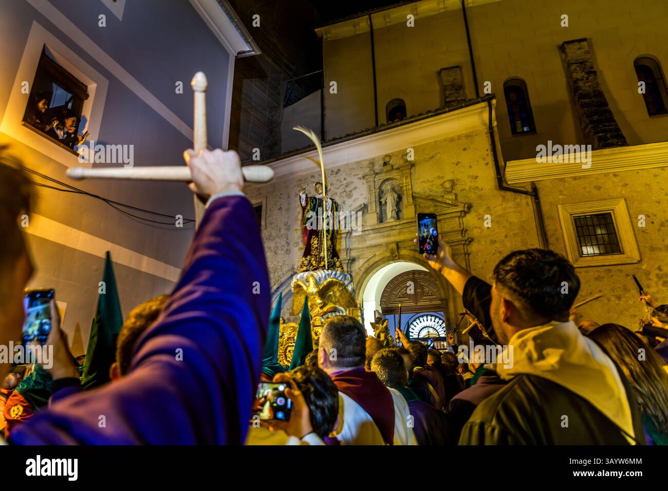 Dense crowds gather in the dark in front of the parish church of El Salvador at the start of the Good Friday procession Camino del Calvario. One participant holds up a wooden cross replica while a saint's statue on a gilded platform waits in the background. The Turbas create a raw noise here meant to reflect the dramatic situation of the Passion. The agitated crowd shouts "Crucify him". Plaza Salvador, Cuenca, Castilla-La Mancha, Spain. The Turbas tradition dates back to their first procession on 4 April 1616. Members, known as turbos, play homemade drums and blow tin trumpets - the off-key tr Stock Photo
