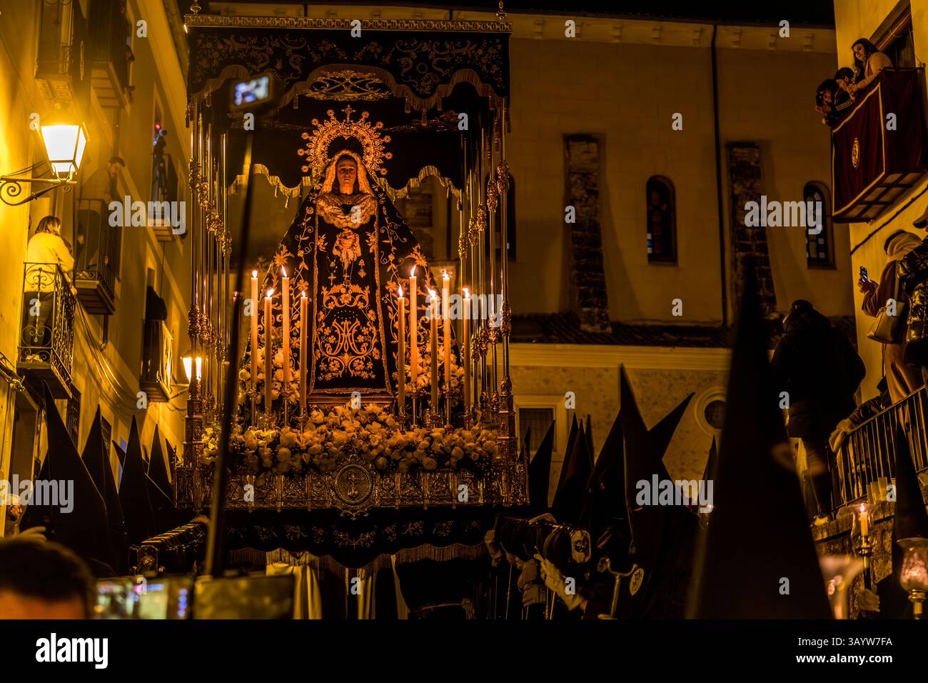 At the sight of the Mater Dolorosa, the paso Nuestra Señora de la Soledad, the angry crowd falls silent and mourns together with her. Surrounded by numerous candles and white flowers, the figure of the Virgin is carried by the Venerable Hermandad de Nuestra Señora de la Soledad de San Agustín. Calle Alonso de Ojeda, Cuenca, Castilla-La Mancha, Spain. The paso, created in 1947 by Federico Coullaut-Valera, depicts the Mother following her Son's steps towards Calvary and is carried by 30 men. During Semana Santa in Cuenca, 33 Hermandades take part in eleven processions through the city during Hol Stock Photo