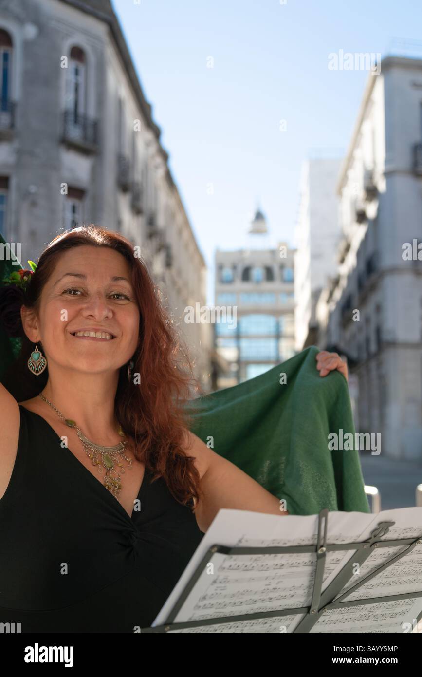 Singing woman holds a green cloth with open arms and smiles at a lectern on a street esplanade. Stock Photo
