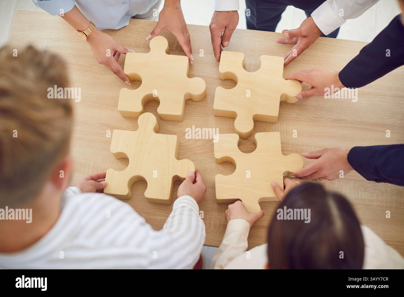 Group of people holding pieces of a large wooden puzzle over a table, top view Stock Photo