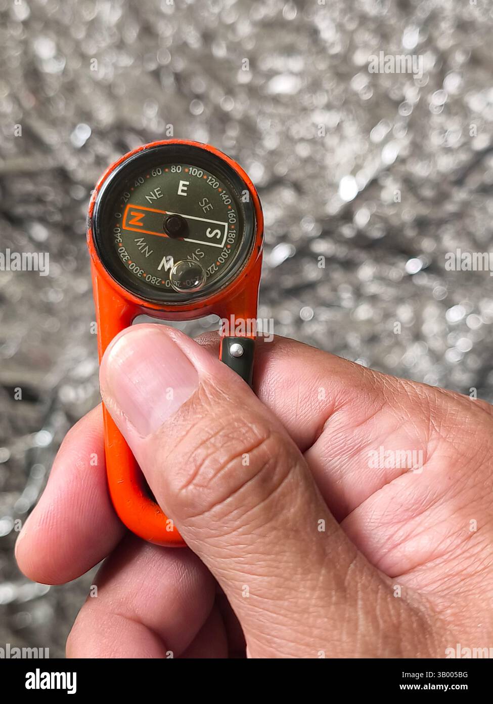 a hanging compass held in the right hand with silver background Stock Photo