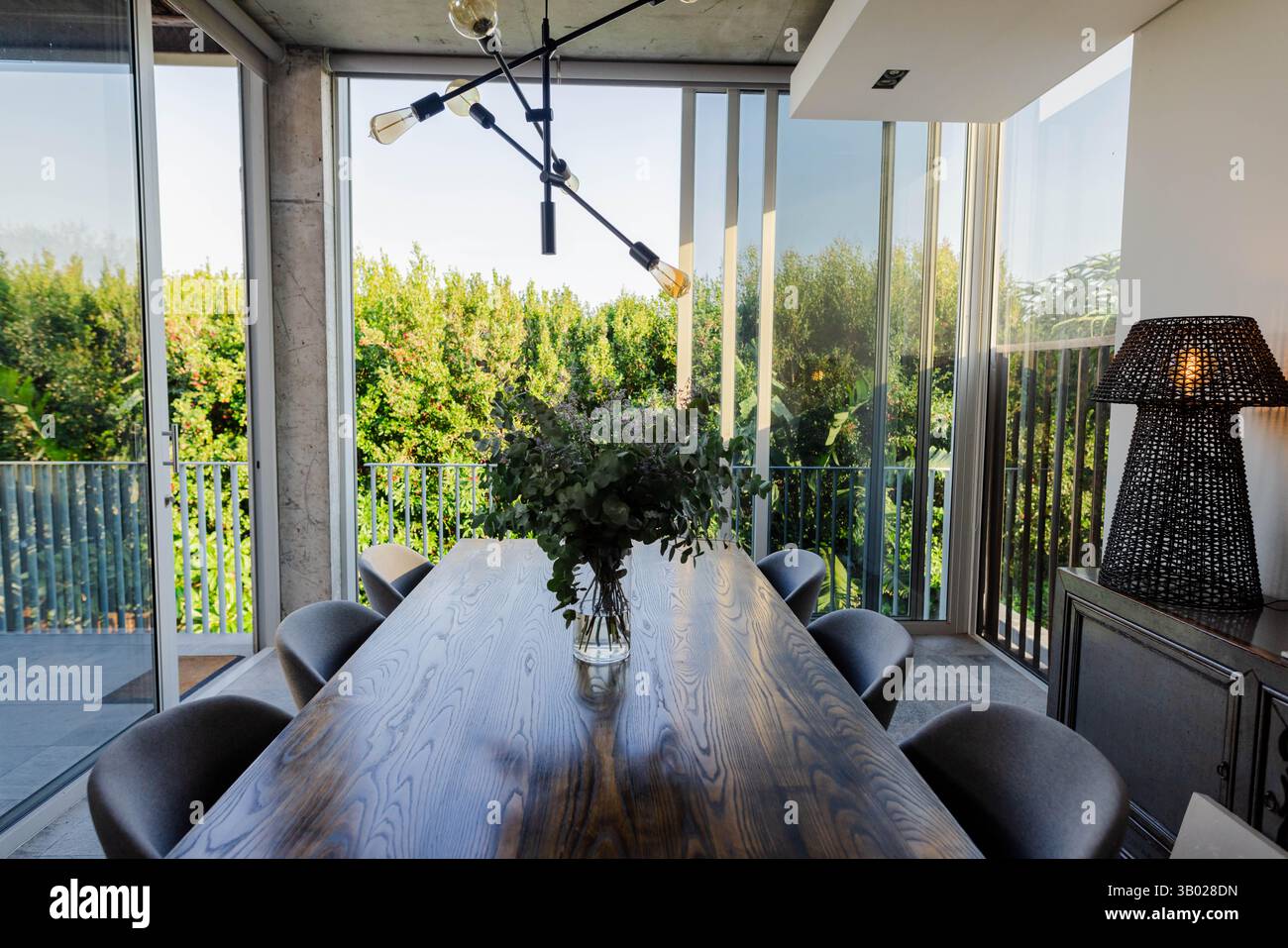 Long dining table is featuring glass vase with green foliage beside sliding doors in dining room ...