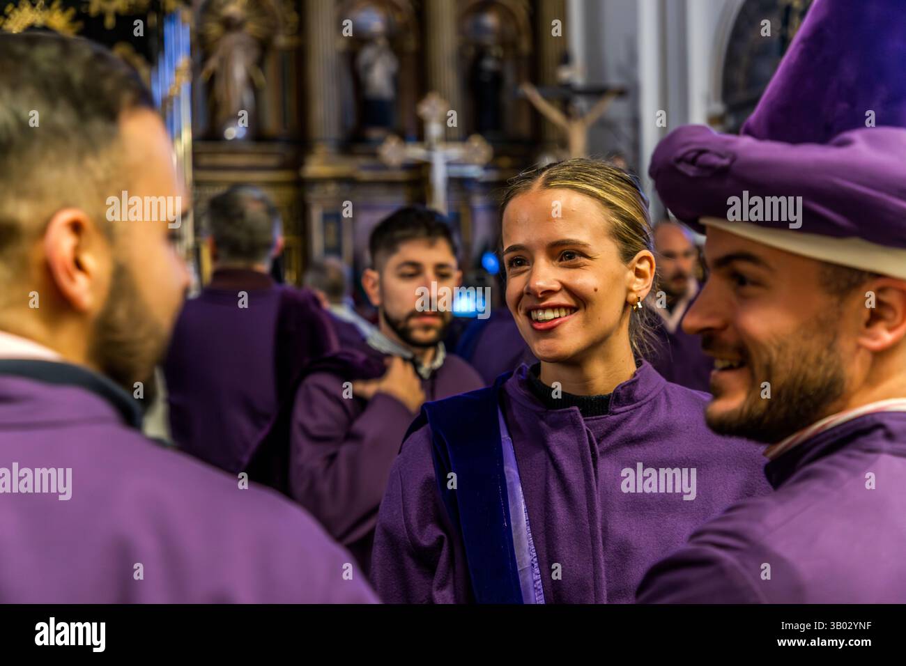 Members of the Camino del Calvario procession prepare in the parish church of El Salvador, Cuenca, Castilla-La Mancha, Spain. Bearers in purple robes and tall pointed hoods gather before the Good Friday procession, their expressions ranging between anticipation and quiet reflection. During Semana Santa in Cuenca, 33 Hermandades take part in eleven processions through the city during Holy Week. Stock Photo