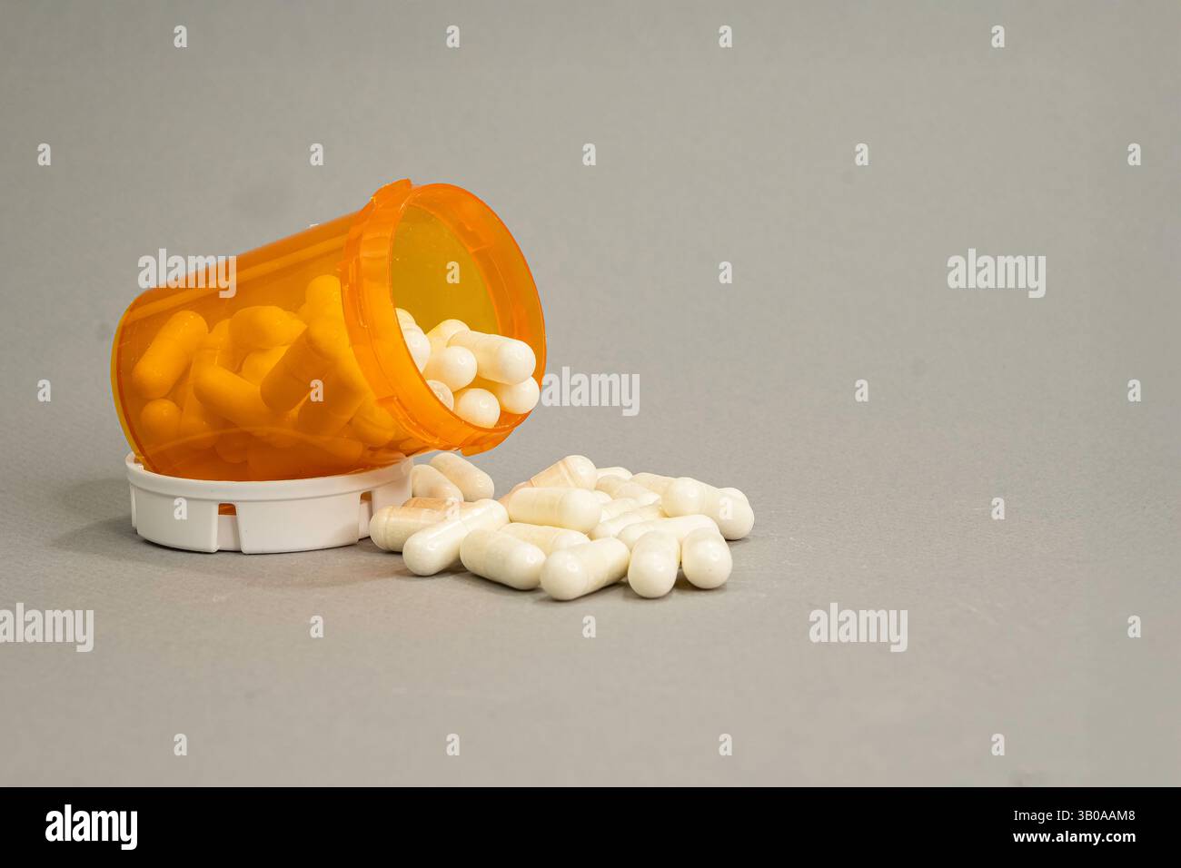 An orange prescription container on its side with capsules spilled out ...