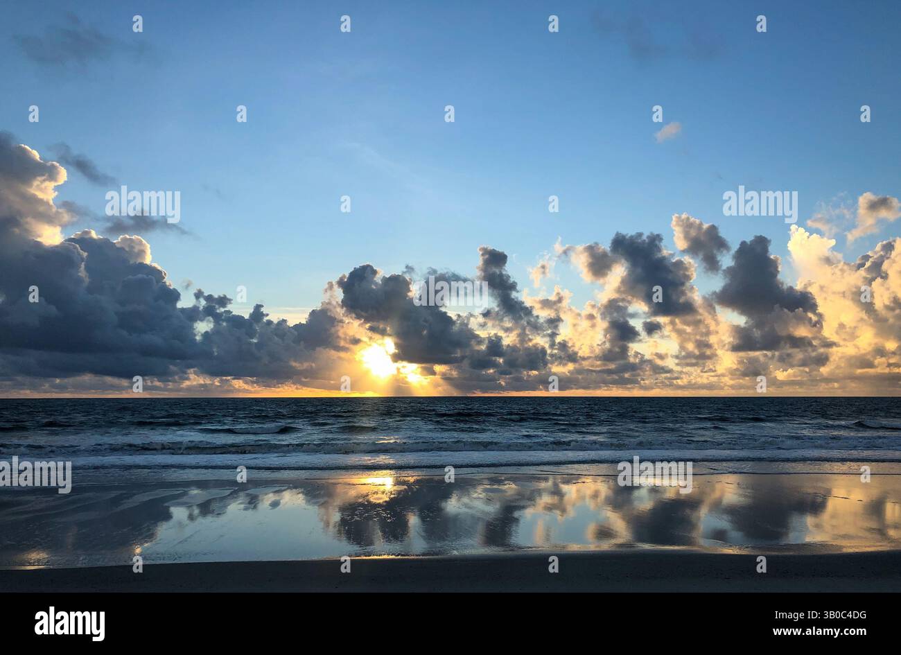 Dramatic clouds with mirror-like images reflected in the shallow water of Amelia Island with sun peaking through the clouds. Florida, USA. - Smartphone Captured Stock Image
