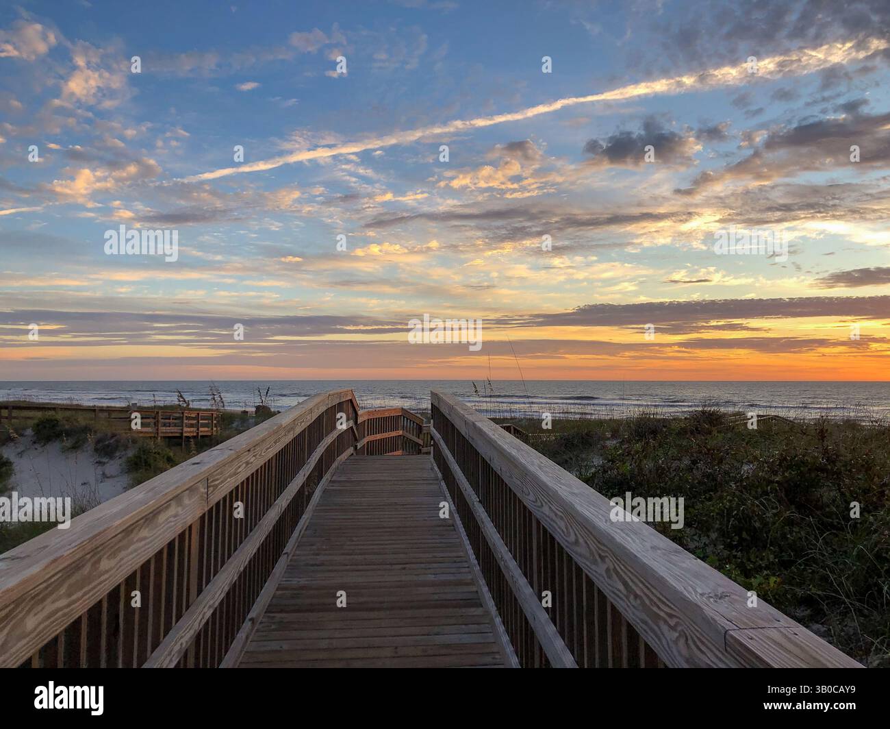 A view of a wooden boardwalk leading to the beach at sunrise with colorful sky and ocean in the background. Amelia Island, Florida, USA. - Smartphone Captured Stock Image