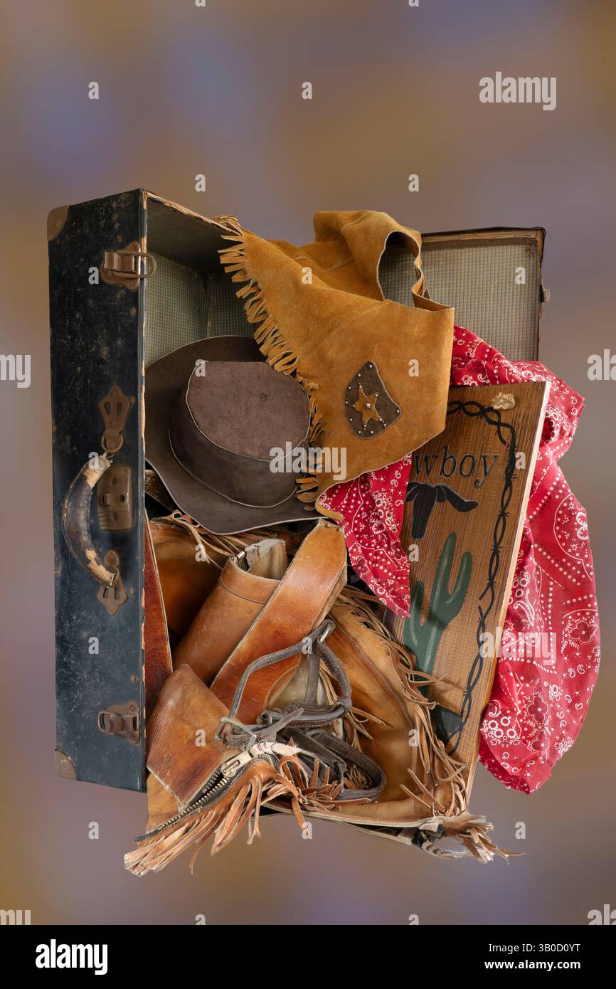 Antique suitcase, handle & latches is open with western gear wear tumbling out. Open antique suitcase stands on end with old cowboy western clothes. Stock Photo
