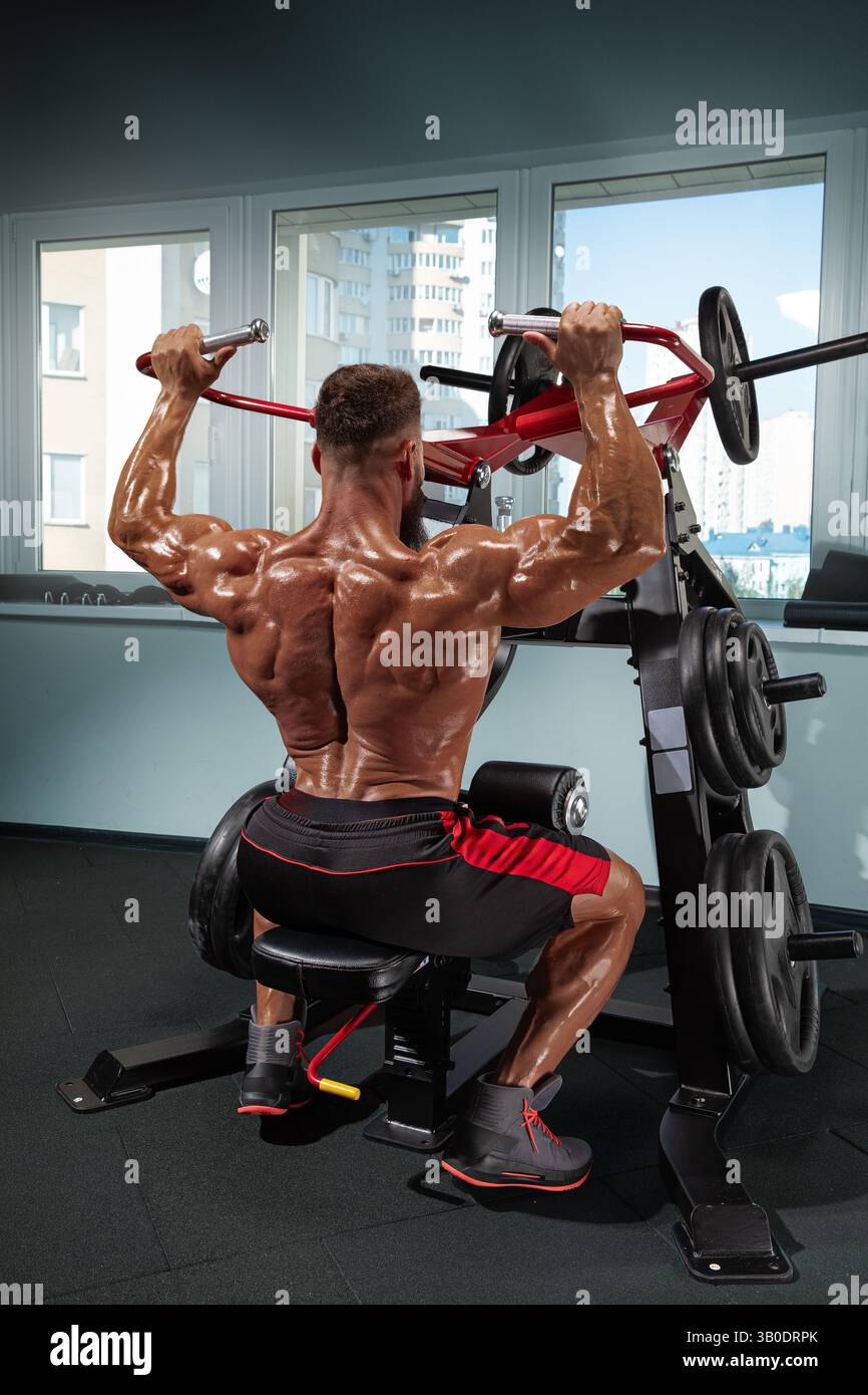 muscular man performs shoulder press on weight training machine in ...