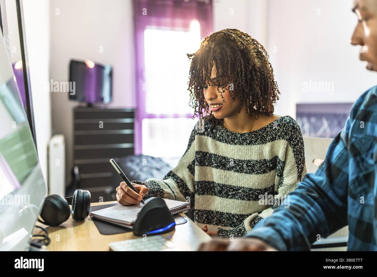 Two programmers working from home, writing notes on notepad while looking at computer screen Stock Photo