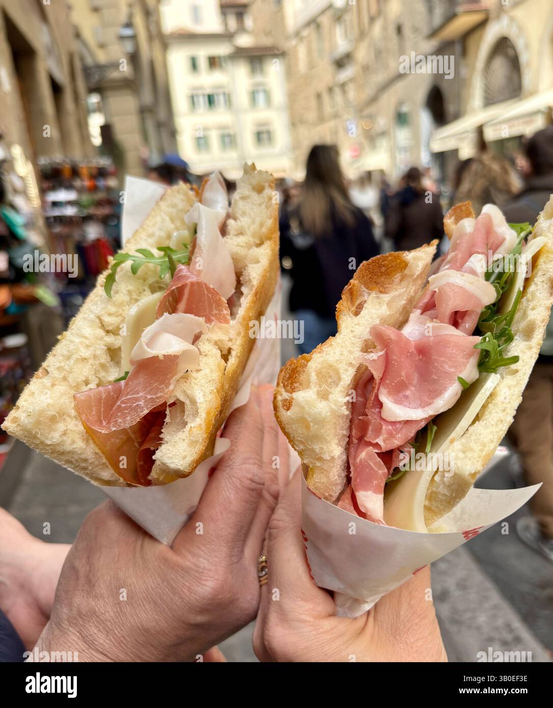 Italian street food.Hands holding a delicious focaccia sandwiches with crispy crust, prosciutto, pecorino cheese and rocket in Florence,Italy. Closeup Stock Photo