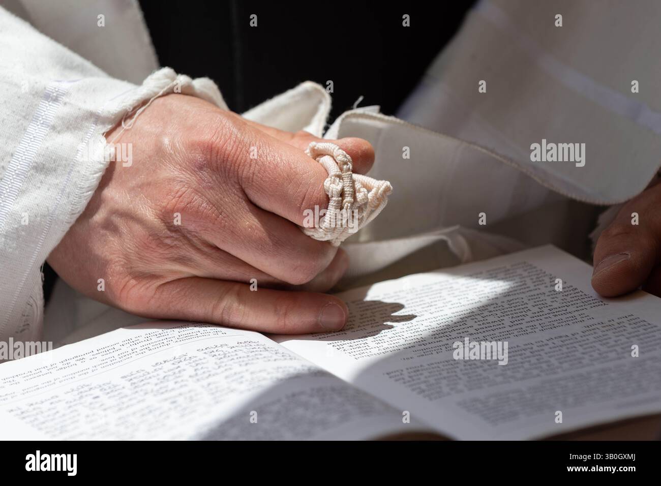 An Orthodox, Jewish man holds tzitzit strings while reciting the Shema