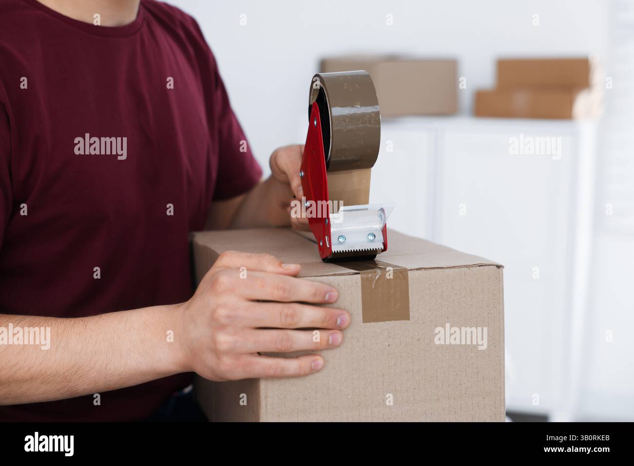 Man using dispenser with adhesive tape to seal cardboard box indoors, closeup Stock Photo