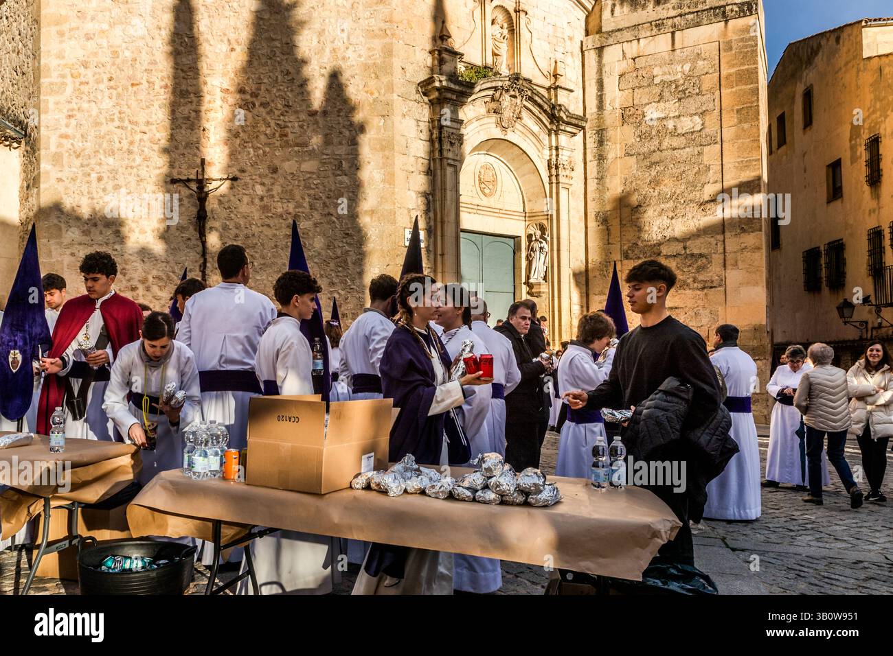 Before the Procession of Forgiveness (Procesión del Perdón), numerous members of the Hermandad del Bautismo de Nuestro Señor Jesucristo fortify themselves in front of the church of San Pedro. Hornazo, a bread filled with ham, chorizo and egg, is the typical marching snack of the costaleros. Calle Trabuco, Cuenca, Castilla-La Mancha, Spain Stock Photo