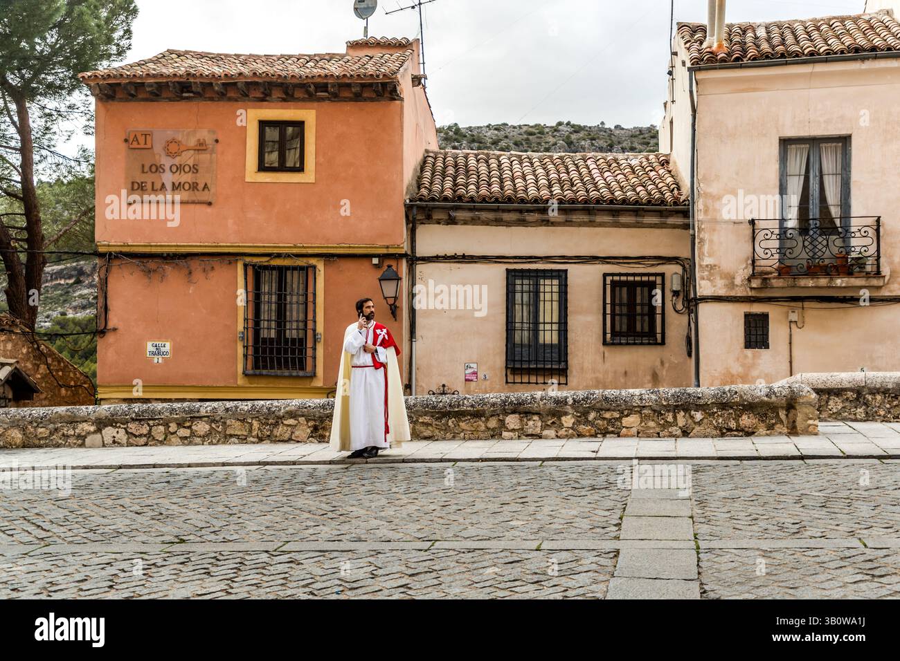 A member of the Hermanidad de San Pedro Apósto in Spanish garb makes a phone call before the procession in Cuenca. Calle San Pedro, Cuenca, Castilla-La Mancha, Spain Stock Photo