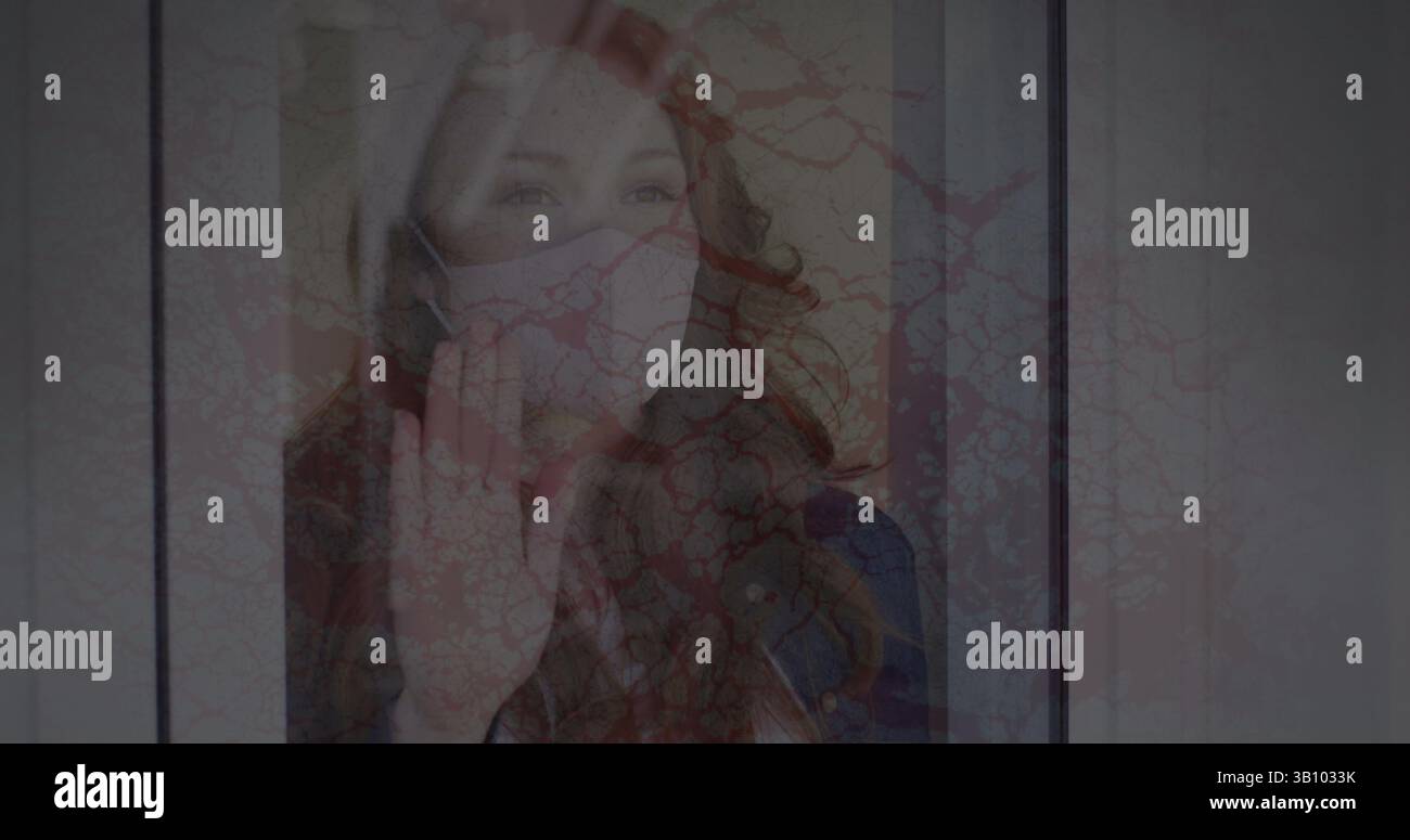 Image of cracked texture changing over sad biracial woman in face mask looking outside window Stock Photo