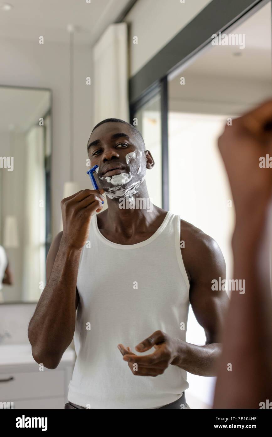 African American man shaving face in modern bathroom, with blue ...