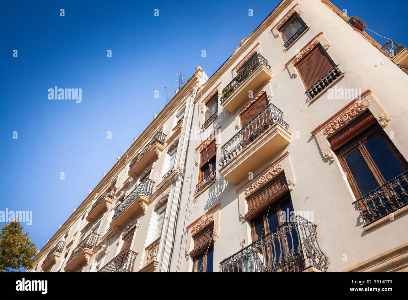 Sun‑lit late‑19th‑century apartment block in Valencia Eixample: ornate plasterwork, wrought‑iron balconies and cream facades rise into a sky, a symbol Stock Photo