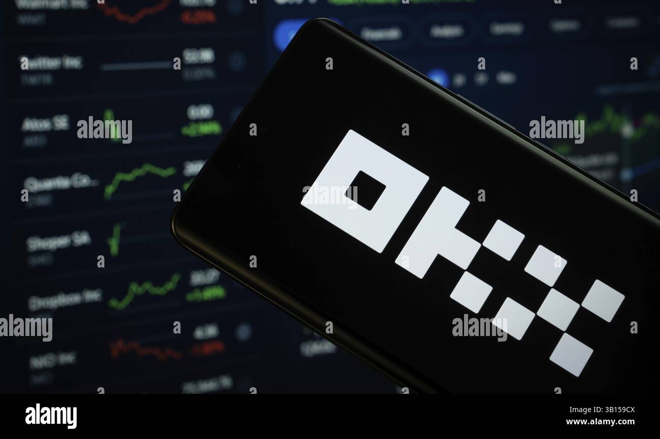 Dhaka, Bangladesh- 17 March 2025: okx logo is displayed on a smartphone screen, with a stock graph webpage visible on a computer screen in the backgro Stock Photo