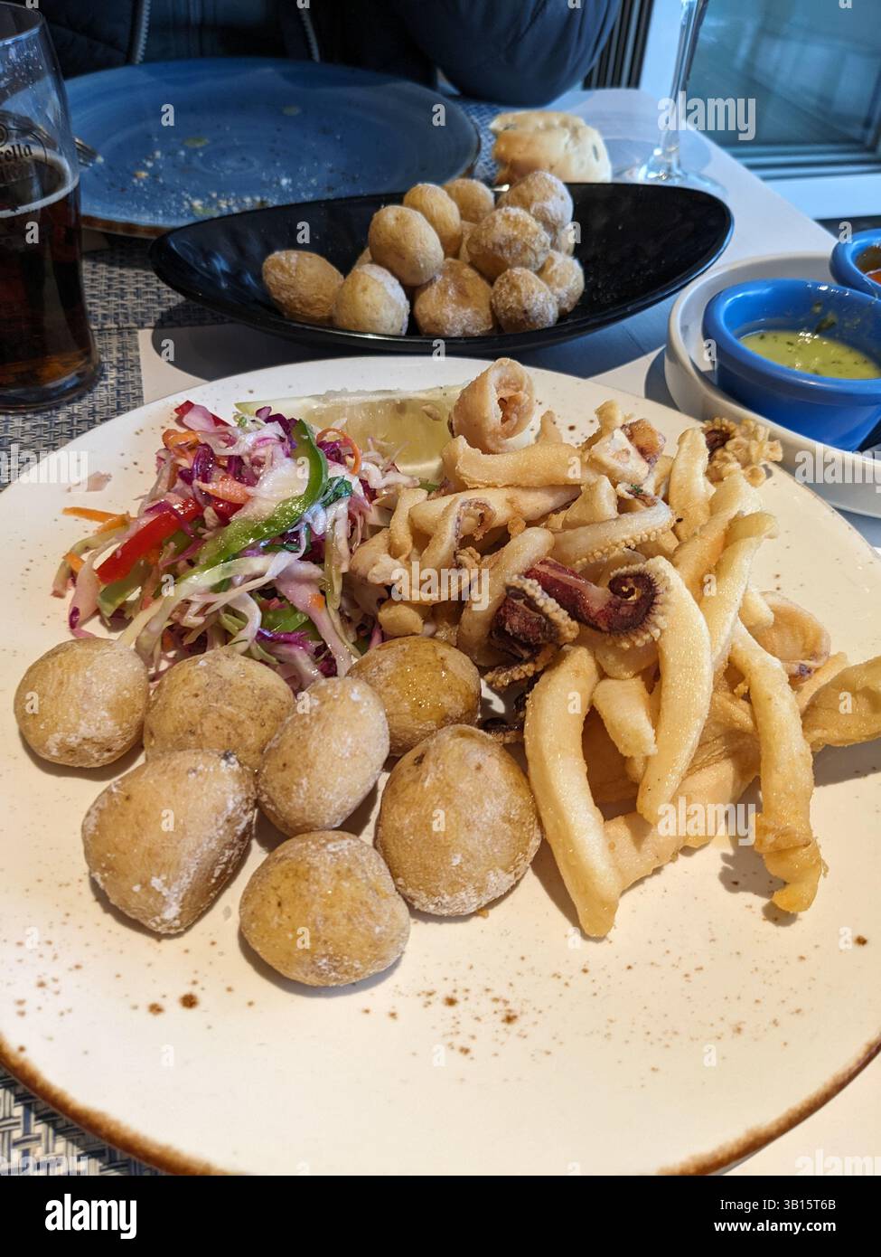 A delicious plate of fried seafood, papas arrugadas, and salad is displayed on a table in a restaurant setting with sauce. Stock Photo