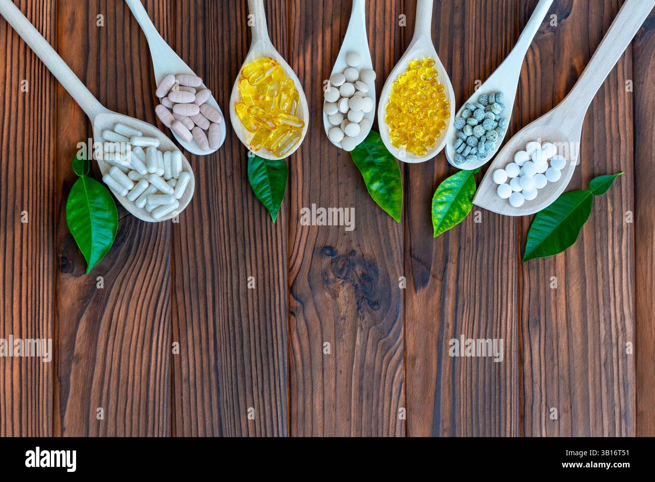 Variety of supplements on wooden spoons with green leaves. Wooden spoons are arranged in a row, each filled with different types of supplements. Top Stock Photo