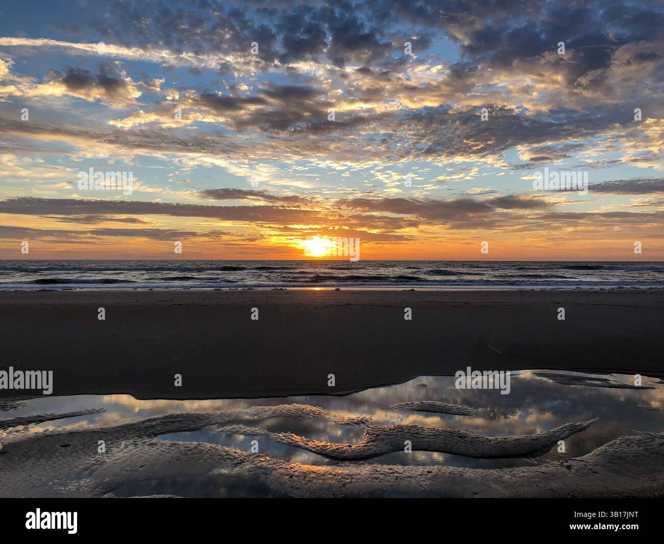 View of a sunrise on Amelia Island with colorful sky, dramatic clouds and a reflection of the sky in the shallow water. Florida, USA. - Smartphone Captured Stock Image