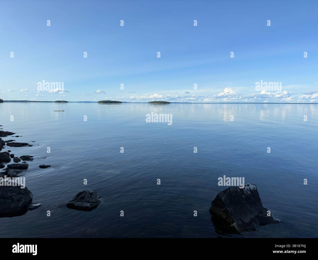 Calm lake scene with reflections on the water, small islands, and a bright blue sky. - Smartphone Captured Stock Image