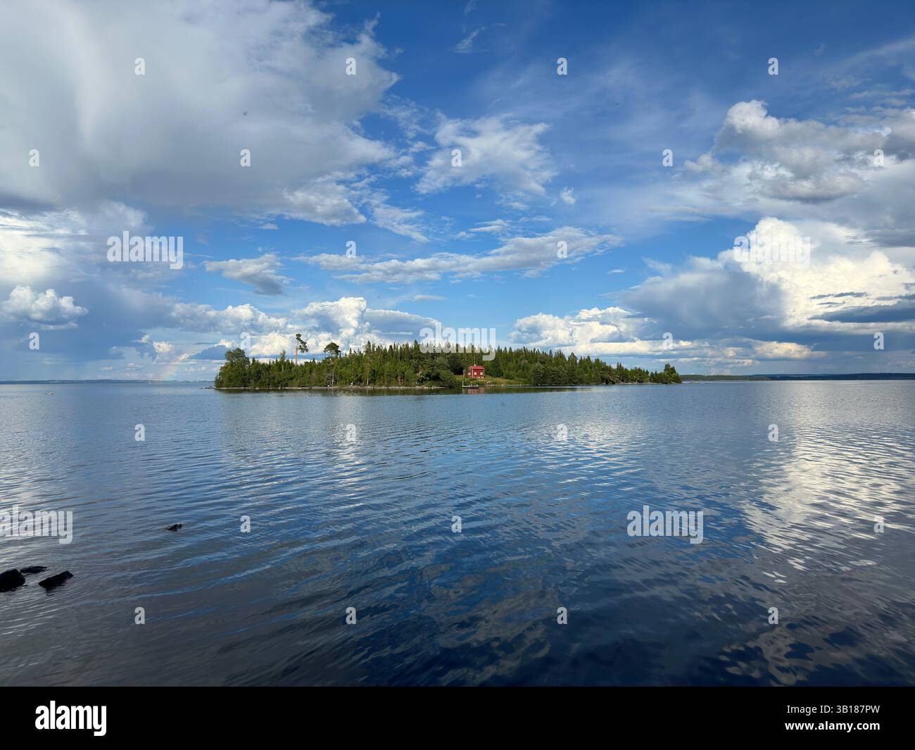 Small island with lush greenery and a red house, surrounded by water under a cloudy sky in Sweden. - Smartphone Captured Stock Image