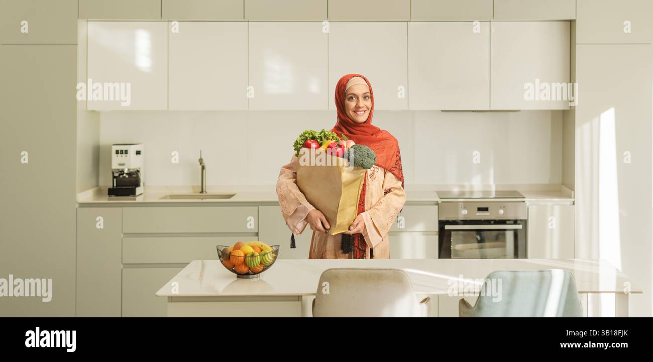 Young muslim woman in a kitchen wearing a hijab and holding a shopping ...