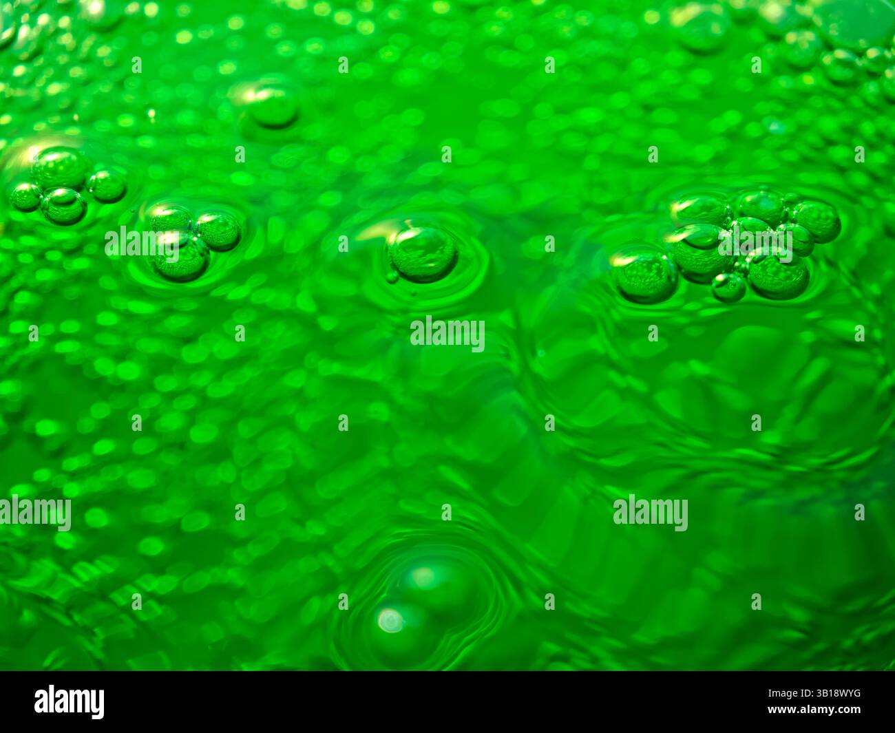 Green bubbly liquid surface forming concentric circles and reflecting light Stock Photo