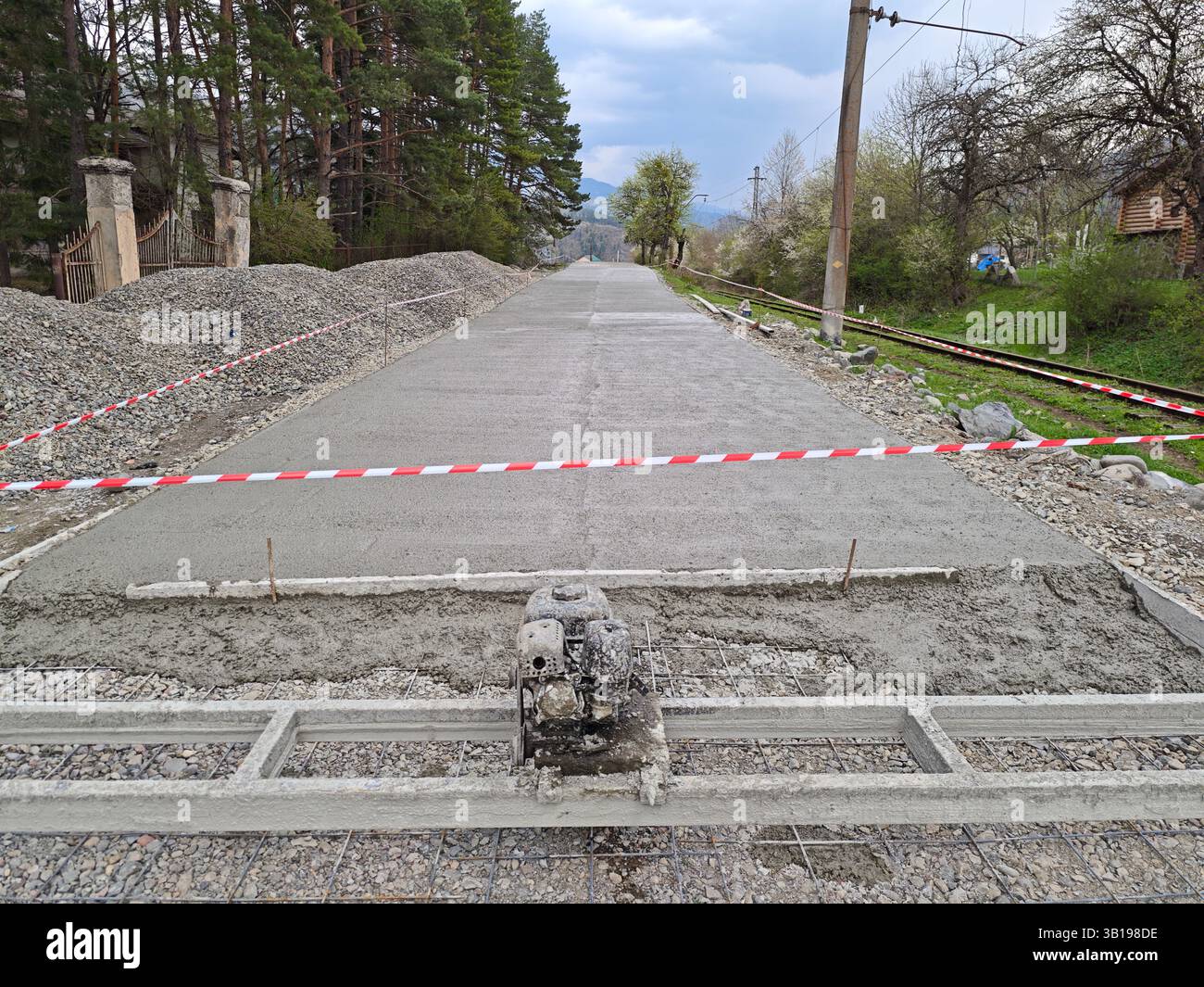 Construction workers building a new concrete road next to railroad tracks, using a concrete vibrator Stock Photo