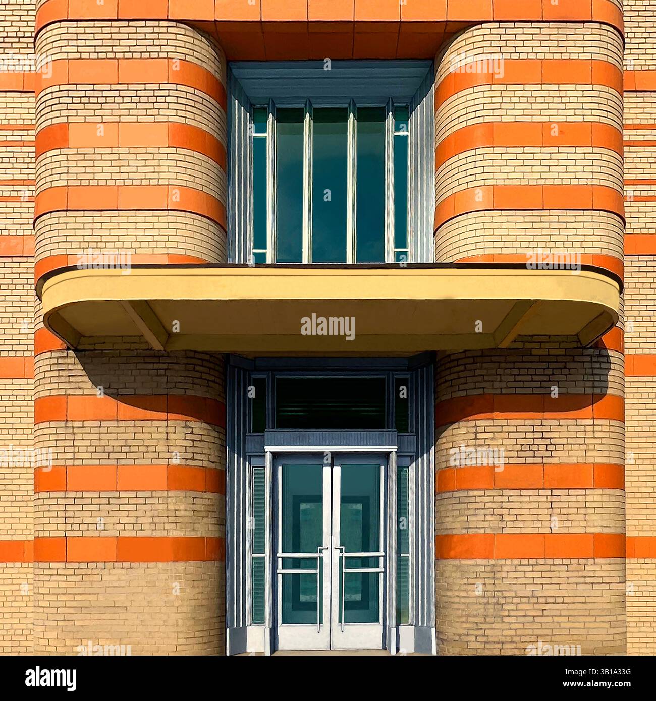 Streamline Moderne Industrial entrance with rounded brickwork, horizontal orange stripes, metal accents, and green double doors in Chicago - Smartphone Captured Stock Image