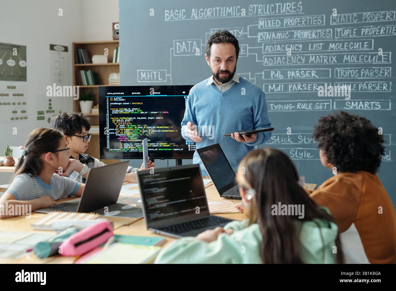 Teacher Guiding Students in Classroom with Computers Stock Photo