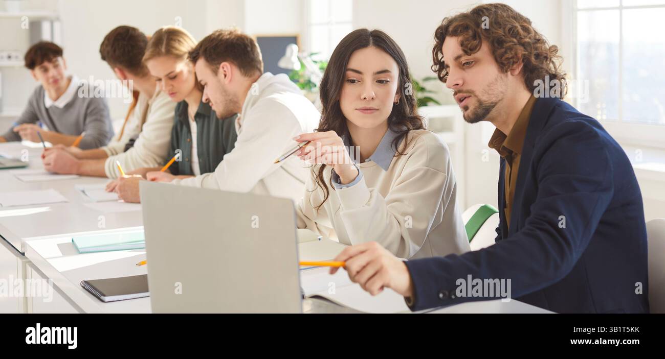 Young students collaborating in modern classroom, discussing project and analyzing data on laptop. Stock Photo