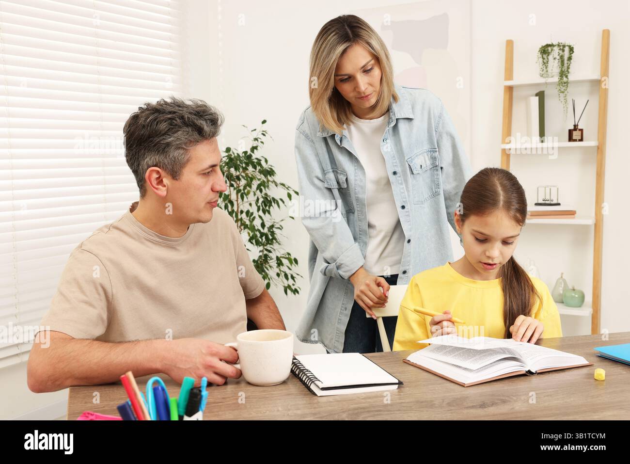 Parents helping their daughter with homework at table indoors Stock ...