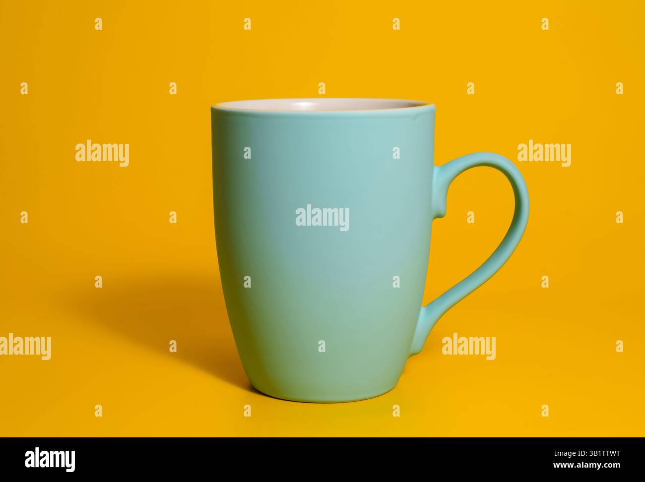 A single matte blue ceramic mug with a handle is placed against a solid yellow backdrop, minimal and clean studio lighting. Stock Photo