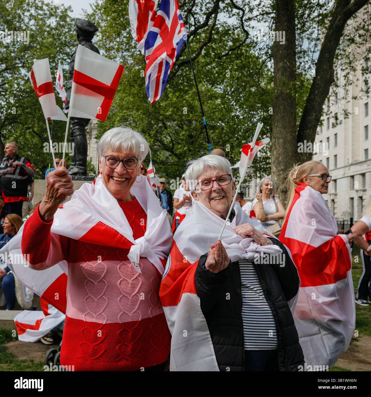 London, UK. 26th Apr, 2025. Two ladies enjoy their afternoon with St George's cross flags and outfits. A crowd of spectators decked out with England flags, and patriotic accessories have assembled opposite Downing Street in Whitehall to celebrate a ' St George's Day Festival' with speakers, performers and music. Some are in full St George's armour and costume. Several of the speakers take a more nationalist tone with political topics such as immigration on the agenda. Credit: News Ldn/Alamy Live News Stock Photo