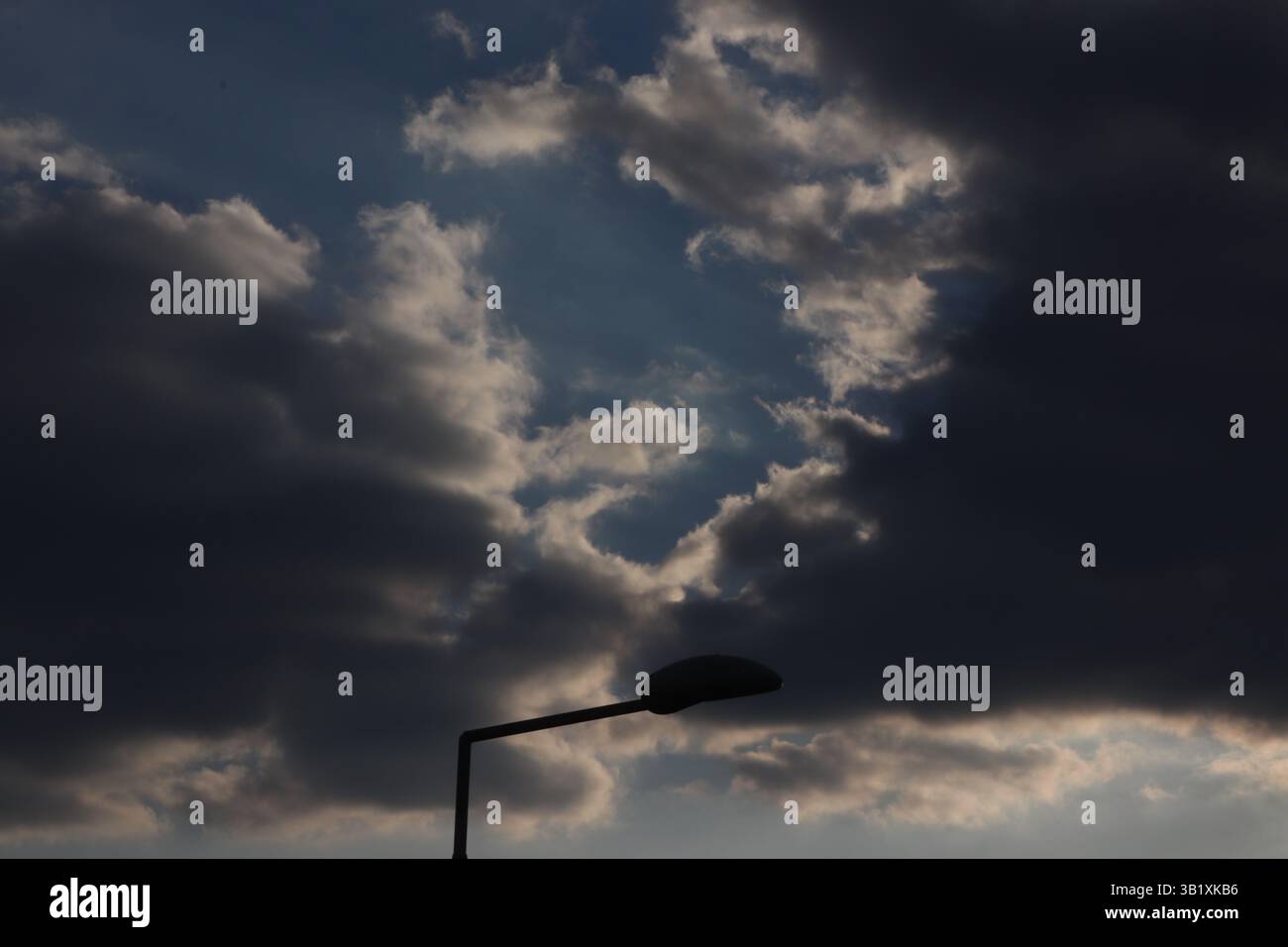 A view of the sky covered by clouds with a lamp silhouette Stock Photo