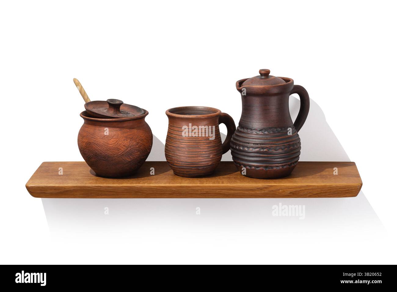Clay jug with handle, pot and mug on oak wooden shelf isolated on white background, front angle view, design element Stock Photo