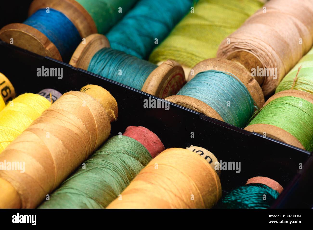 Lot of Colored spools with thread in dark plastic box close up background Stock Photo