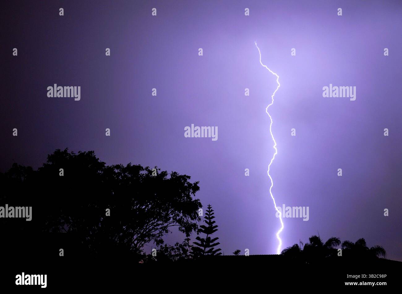 A vivid lightning bolt splits the purple night sky above silhouetted ...