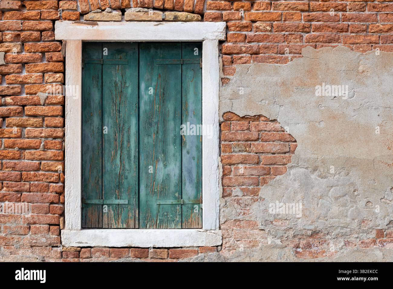 Aged green window shutters on rustic brick wall with peeling plaster Stock Photo