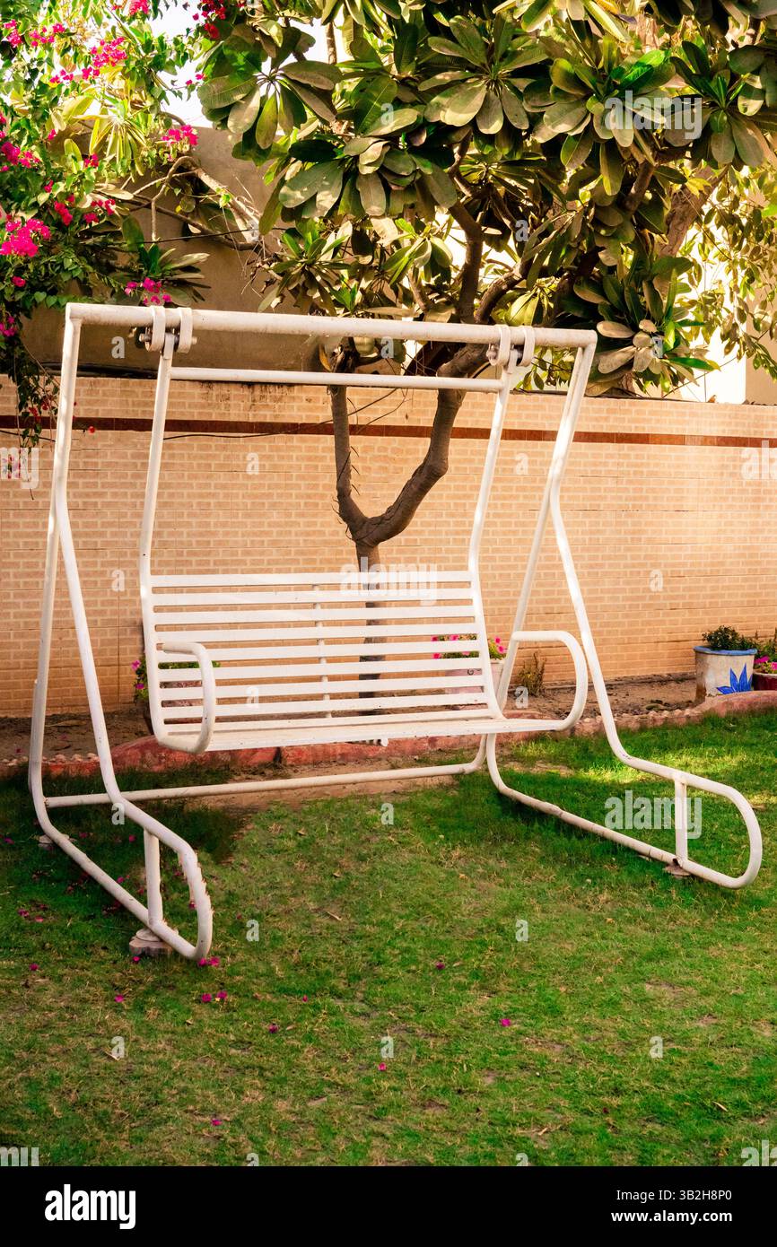 White Swing in a Garden. Concept of relaxation and Peace. aimed greenery Stock Photo