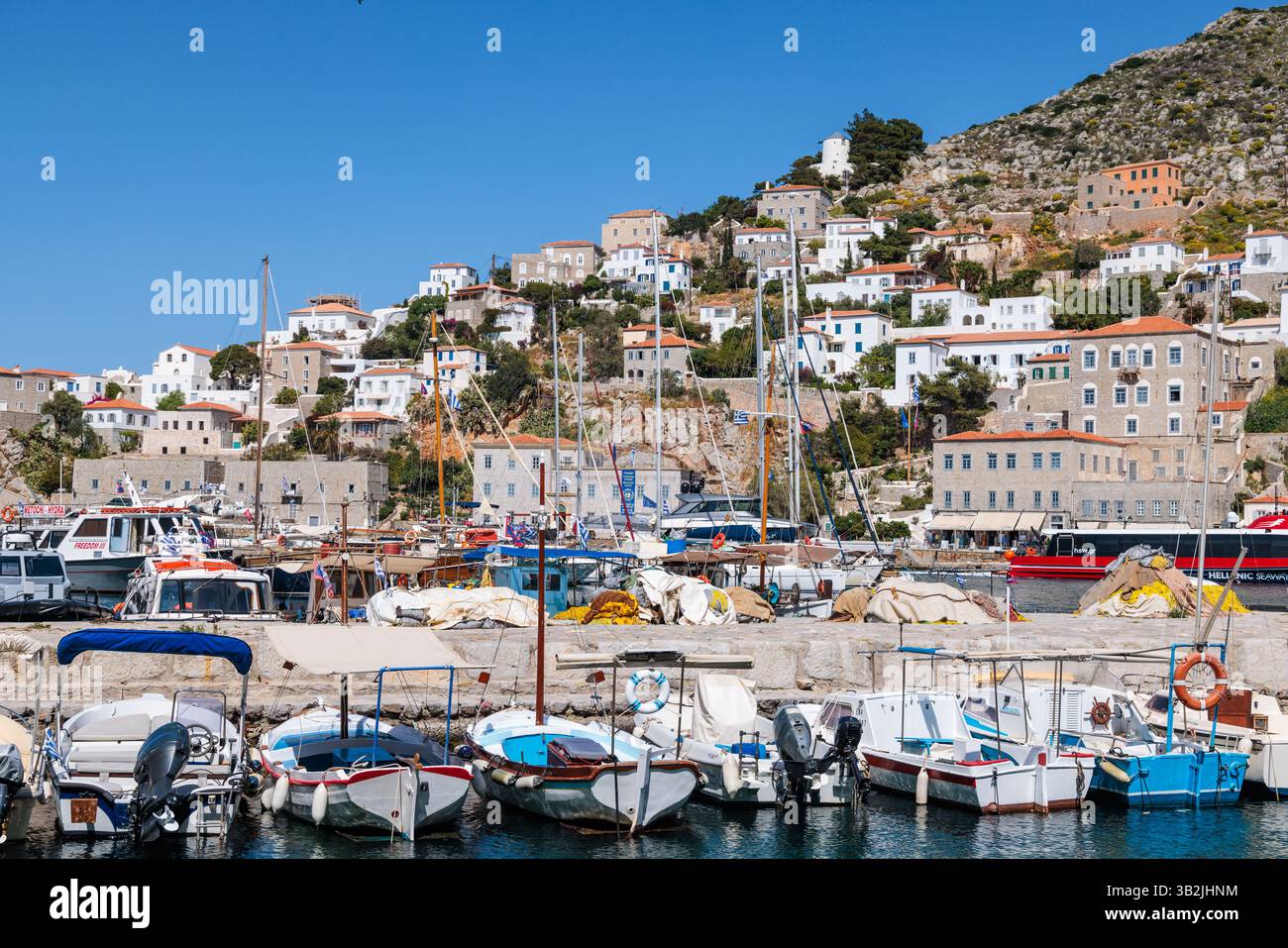 The main harbour in Hydra, Greece, with houses rising up the hill from sea level and boats docked in the foreground. Stock Photo