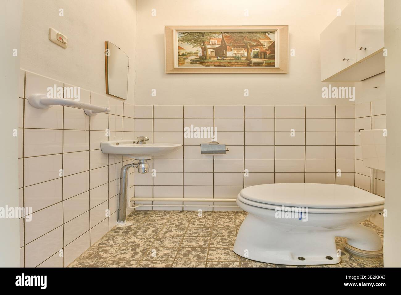 A clean and simple bathroom interior featuring white tiles, a toilet, and a decorative painting on the wall, creating a serene ambiance. Stock Photo