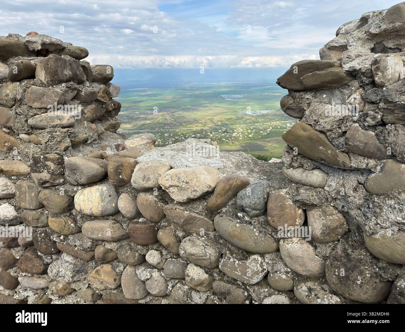 An ancient stone wall with a textured weathered surface, set against the vast open landscape of the Alazani Valley, Georgia. Ideal for history, archit - Smartphone Captured Stock Image