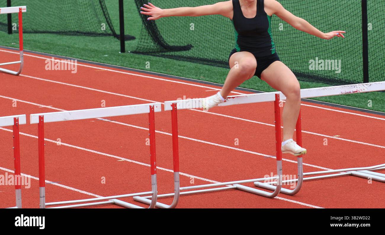 Female high school hurdler jumping over a hurdle during a track race ...