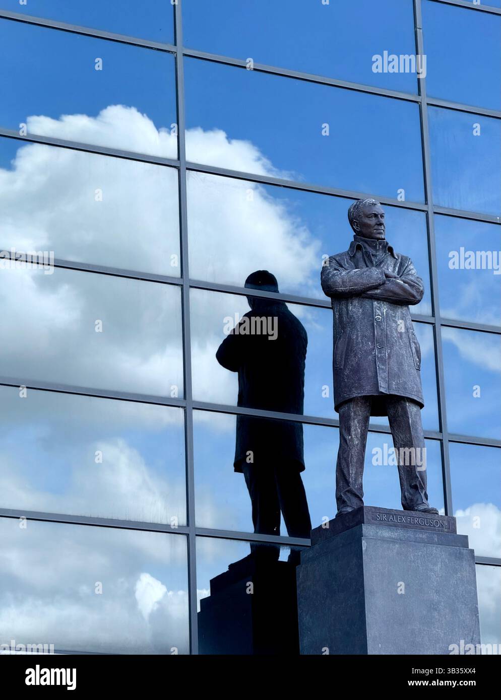 Sir Alex Ferguson stand at Old Trafford football Stadium. Statue with clouds and blue sky reflected in windows of stand. Manchester, uk - Smartphone Captured Stock Image